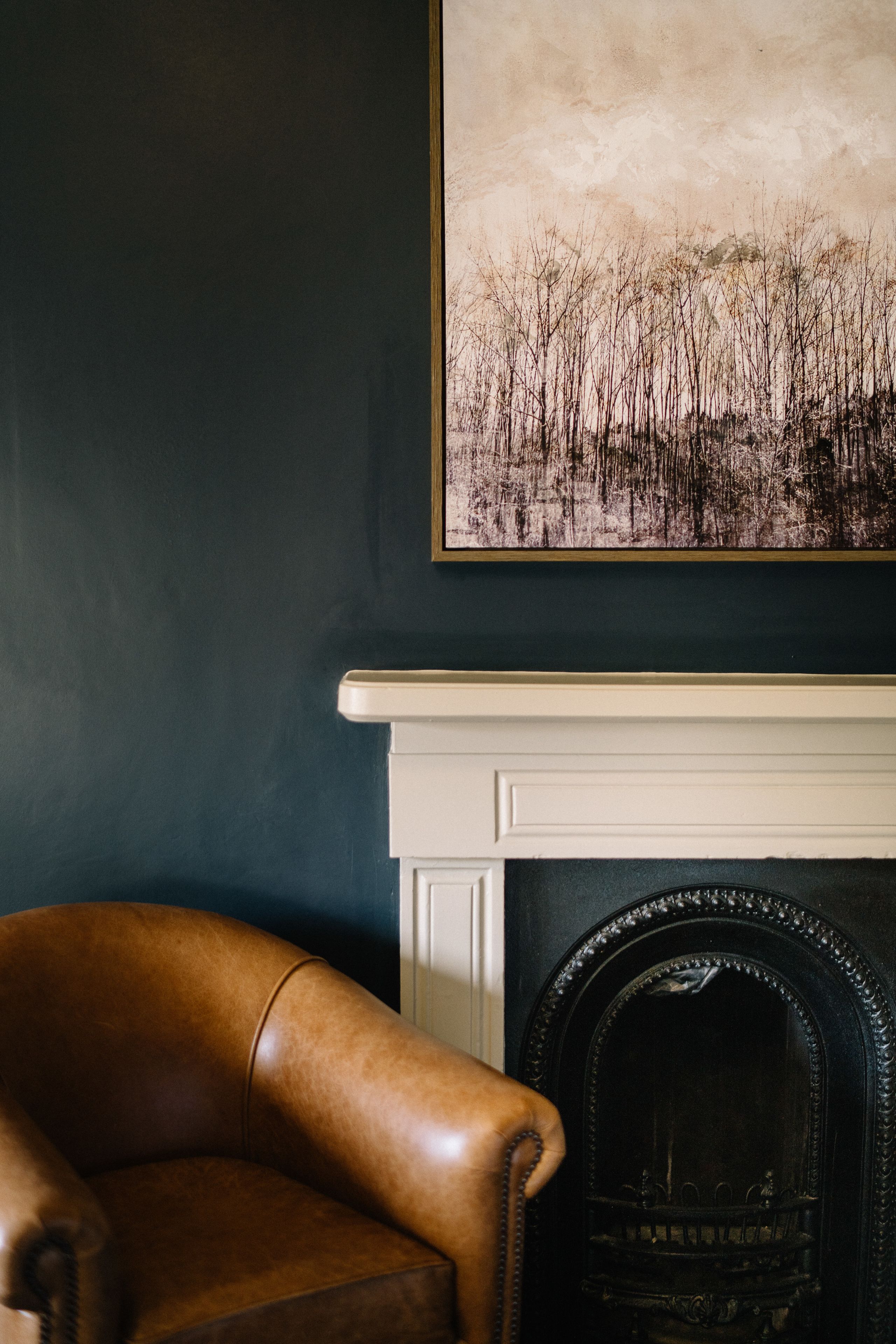 A room with a dark wall, a white fireplace, and a brown leather armchair.