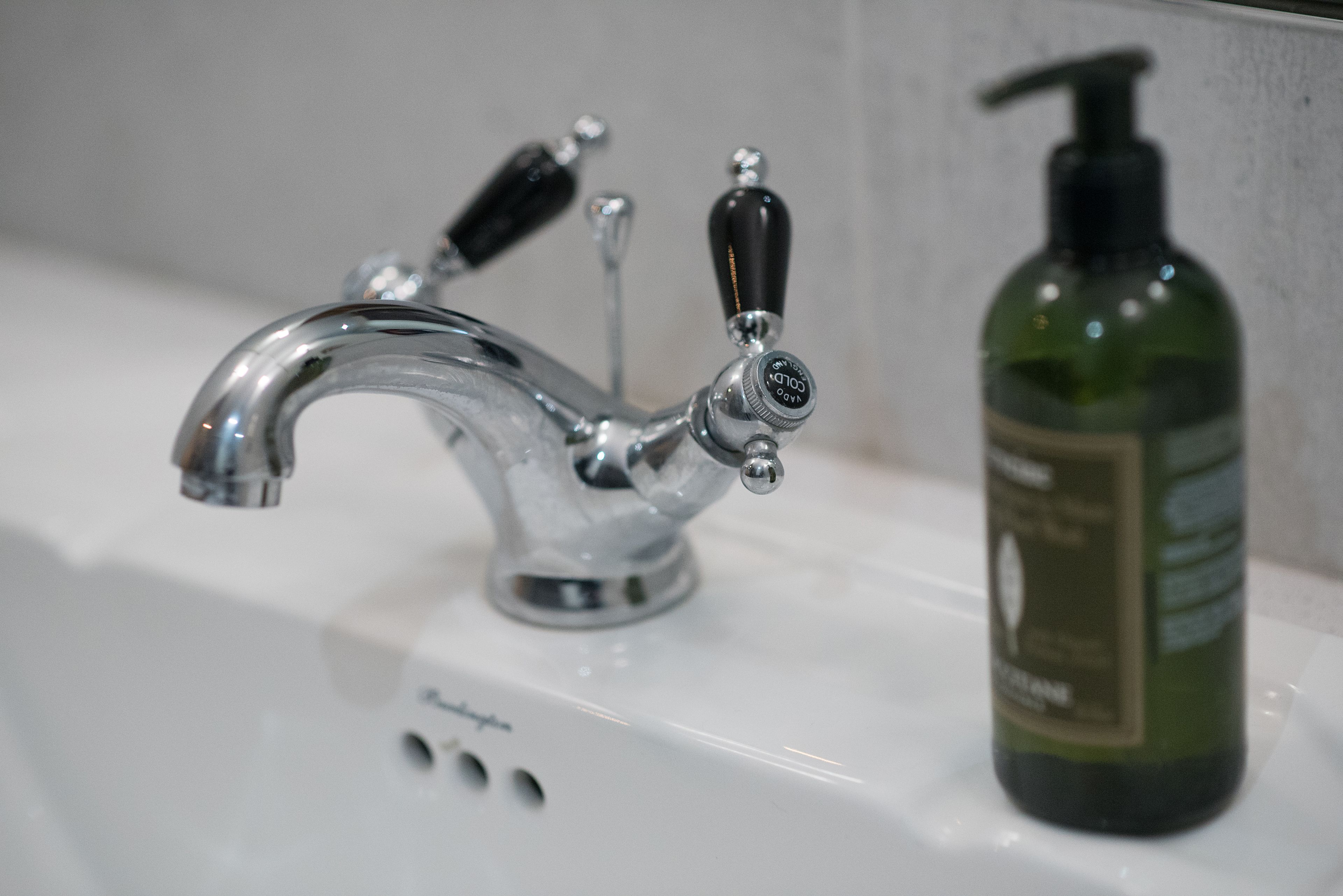 A bathroom sink with a vintage-style faucet and a green bottle of hand soap.