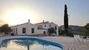 Un área de piscina con patio de piedra, un edificio blanco con varias ventanas y un árbol alto.