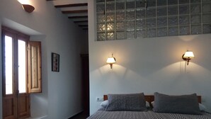Un dormitorio con una cama, dos lámparas de pared, un ventanal con vidrio esmerilado y una puerta de madera.