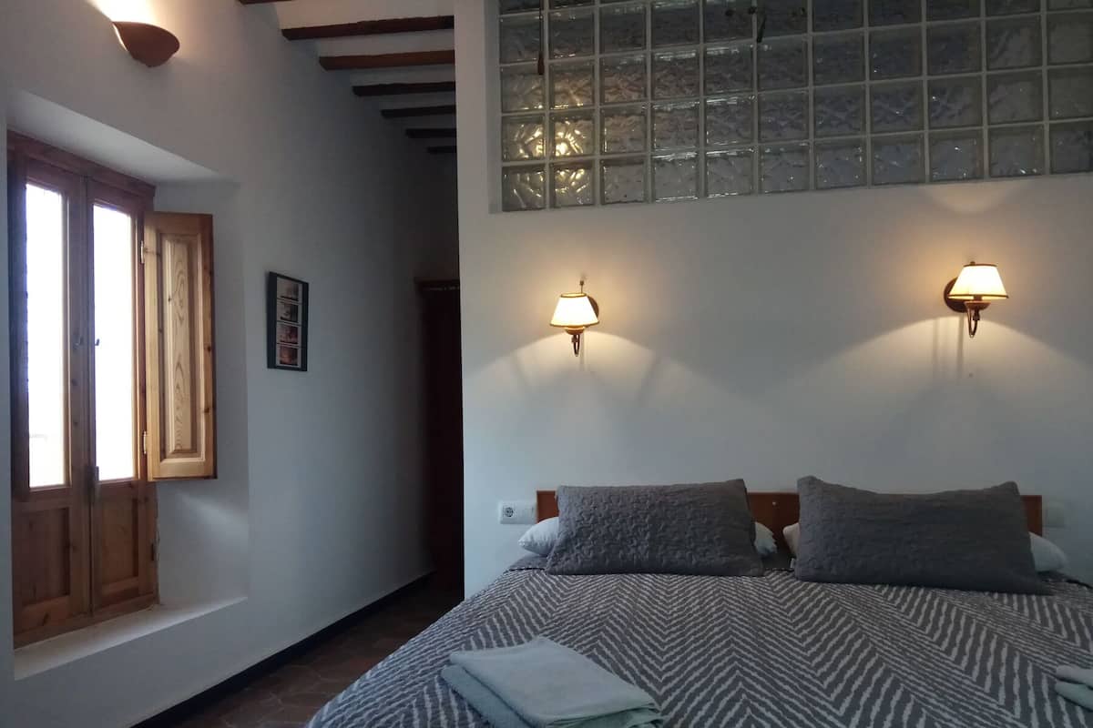 Ein Schlafzimmer mit einem Bett, zwei Wandleuchten, einem Fenster mit Milchglas und einer Holztür.