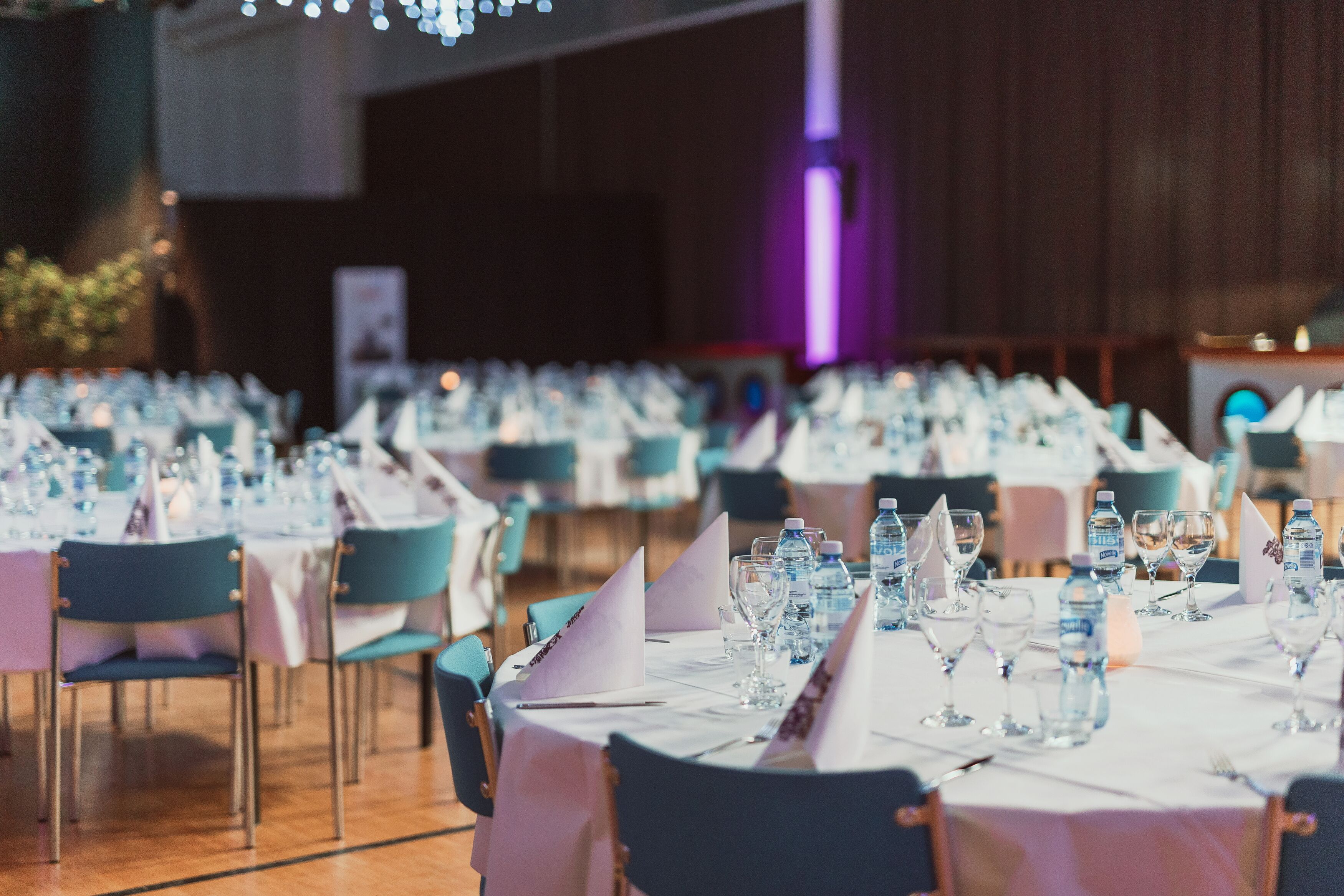 Un salón de banquetes con mesas dispuestas para un evento formal, con manteles blancos y sillas azules.