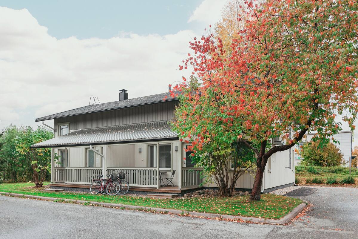 Ein Bungalow mit Veranda, einem Fahrrad und einem Baum mit Herbstlaub.