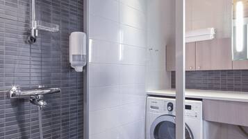 A modern bathroom with a shower, a washing machine, and a trash bin.
