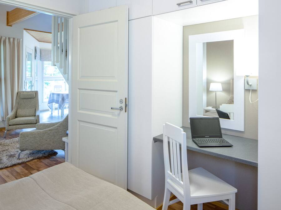 A bedroom with a bed, a desk with a laptop, a chair, and a mirror.