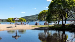 Ein See mit Strand, einem Pavillon, Bäumen und Menschen, die am Wasser entspannen.