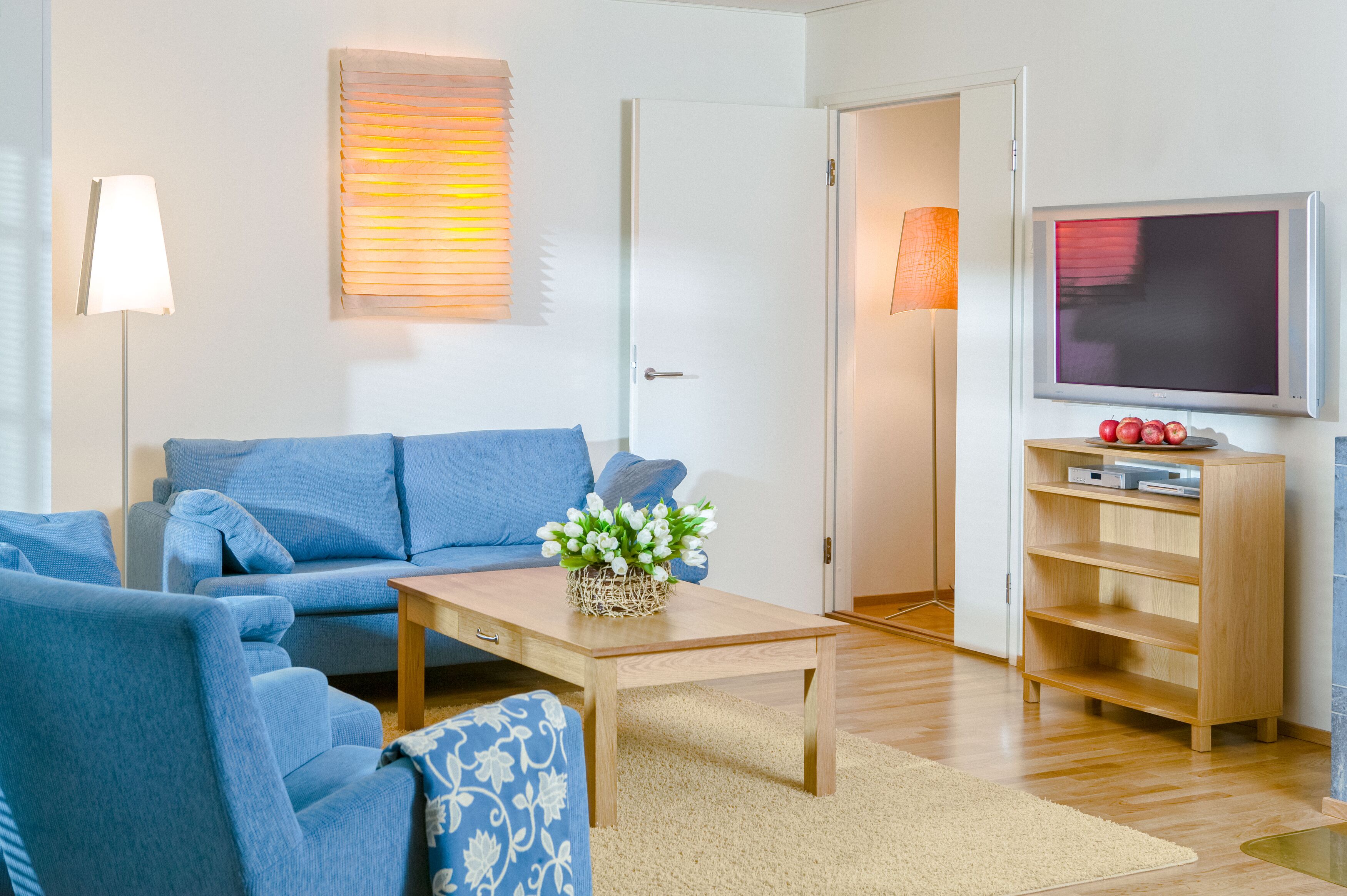Una sala de estar con un sofá azul, una mesa de centro de madera y un televisor sobre un mueble.