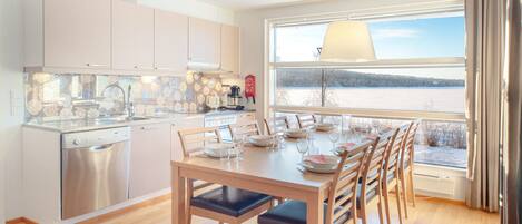 A modern kitchen with a dishwasher, a dining table set for six with chairs, and a large window overlooking a snowy landscape.