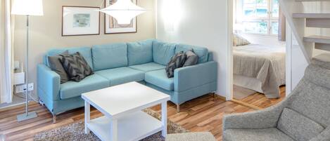 A modern living room with a light blue sectional sofa, a white coffee table, and a grey armchair. There is a large window providing natural light and a view of the outdoors.