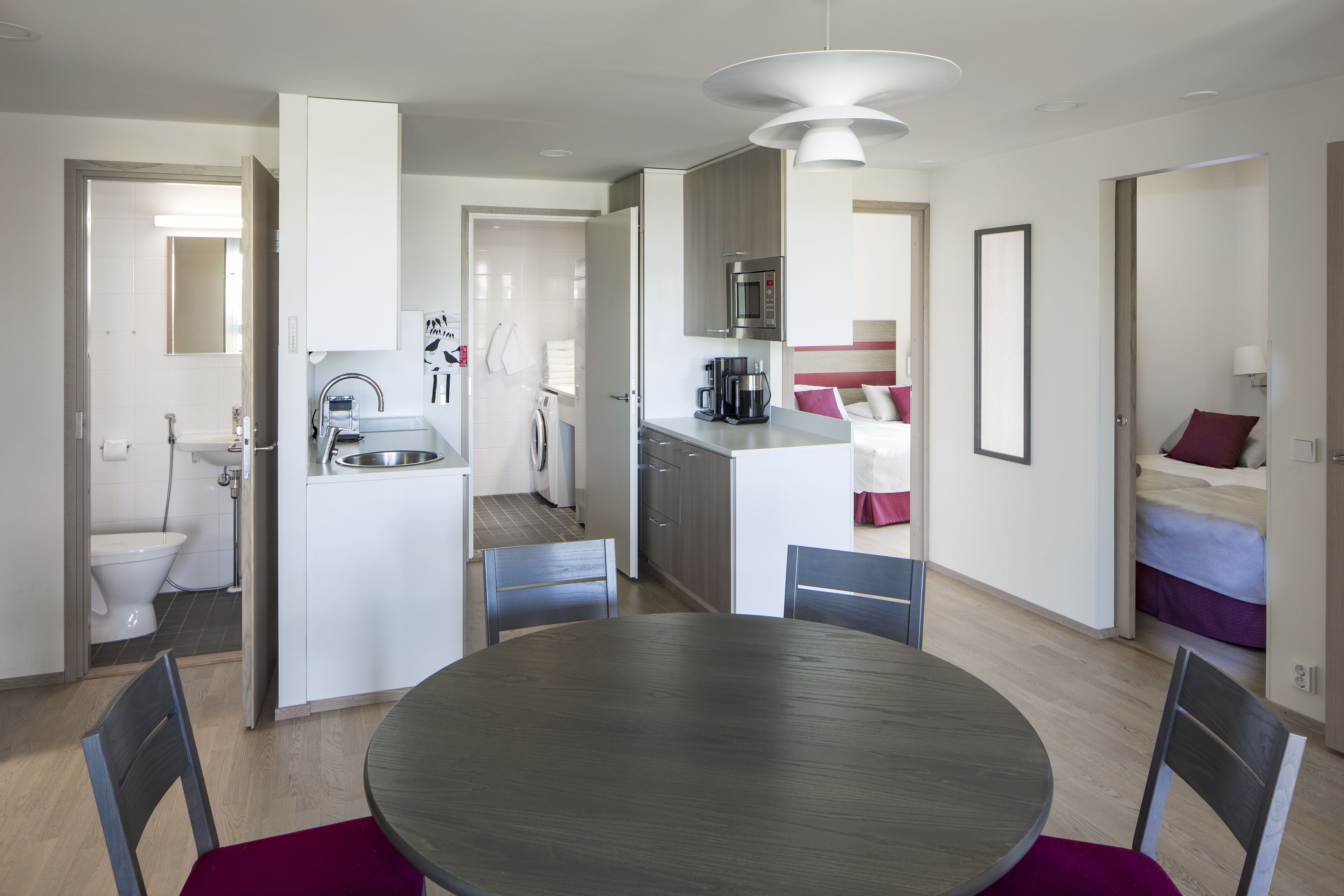 A modern kitchen with a central island, a dining area with a round table and chairs, and a separate bedroom with a bed and nightstand.