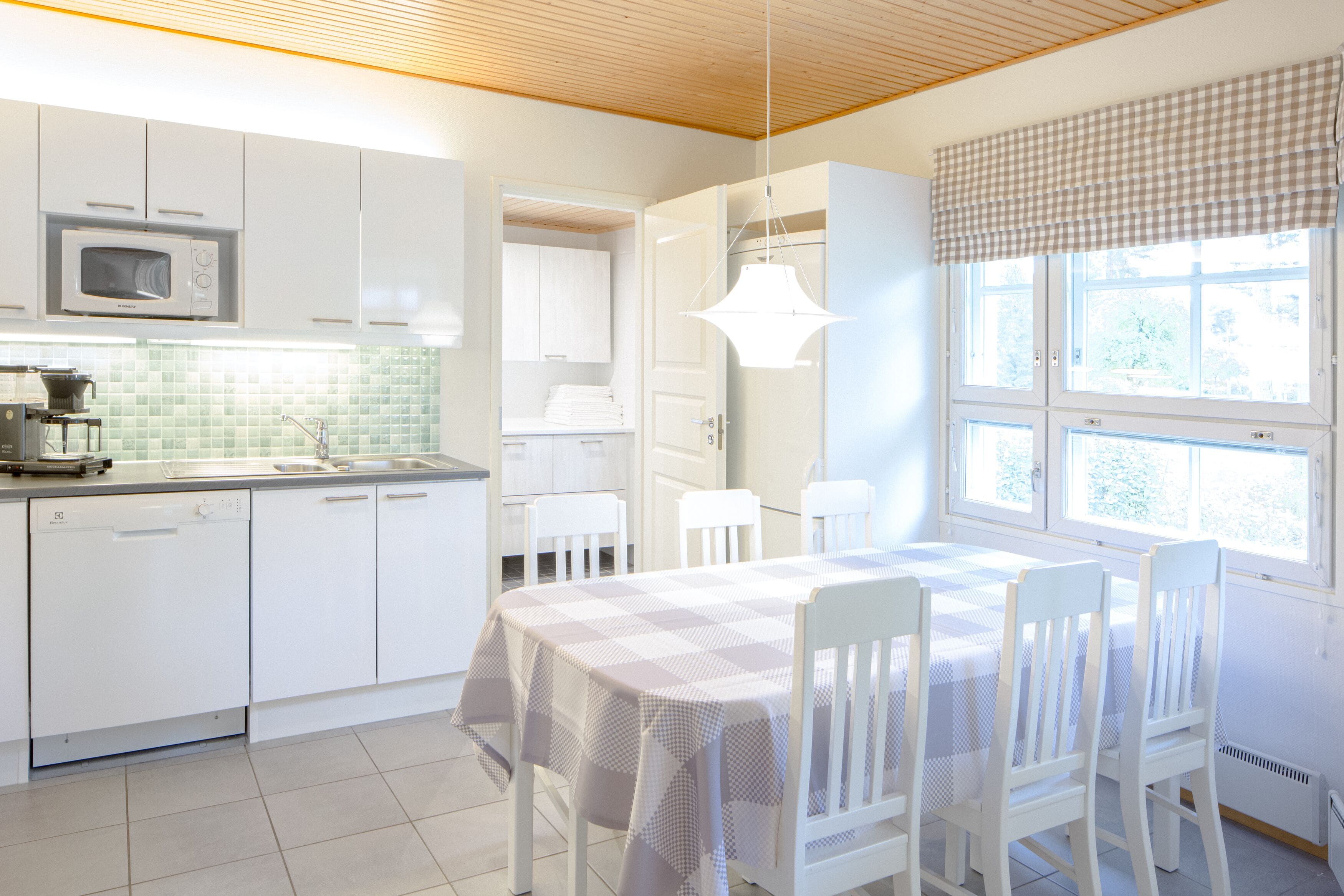 A bright kitchen with white cabinets, a microwave, and a dining area with a checkered tablecloth.