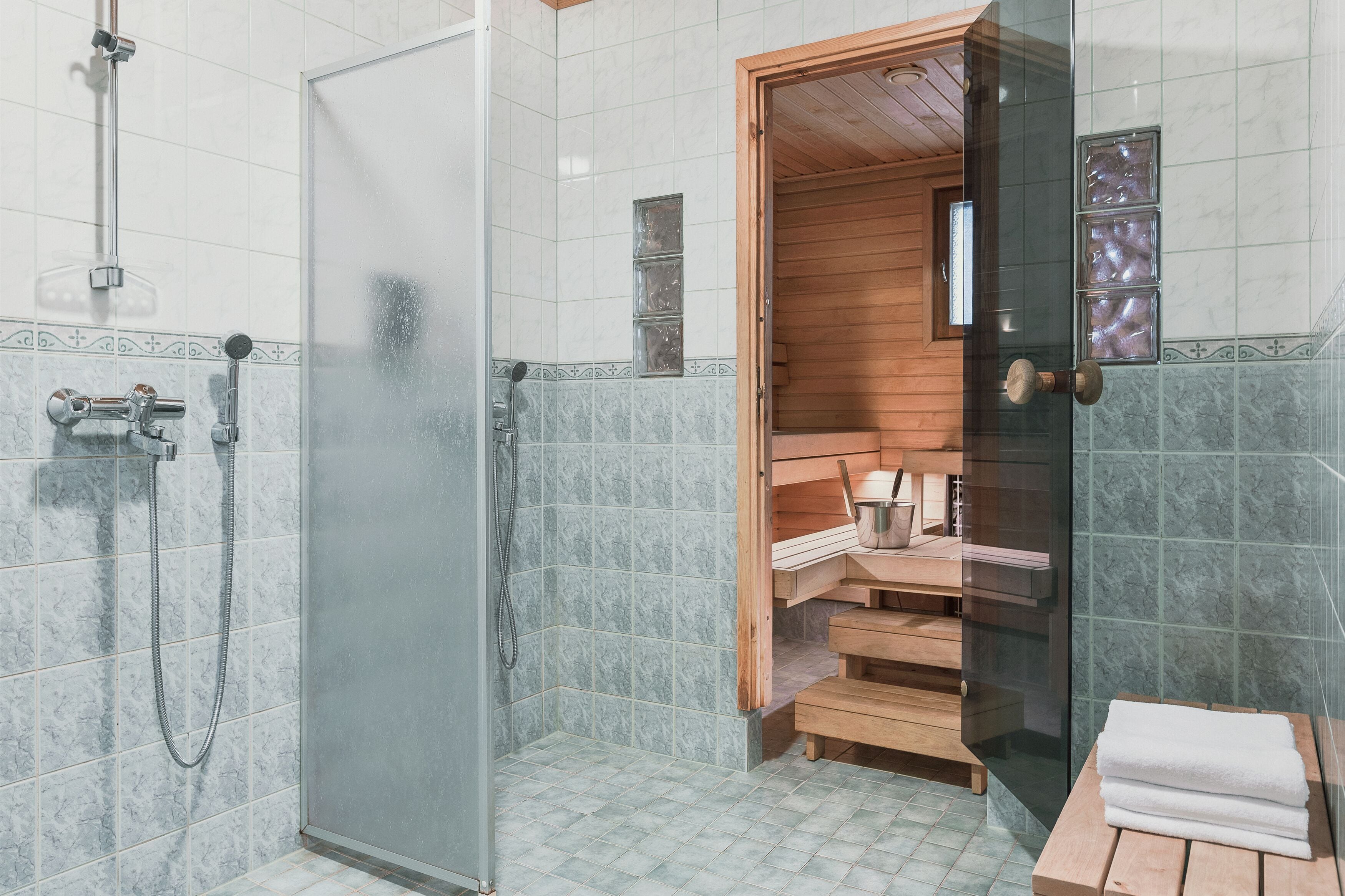 Een moderne badkamer met een douchecabine van glas, een houten sauna en een klein zitgedeelte met handdoeken.