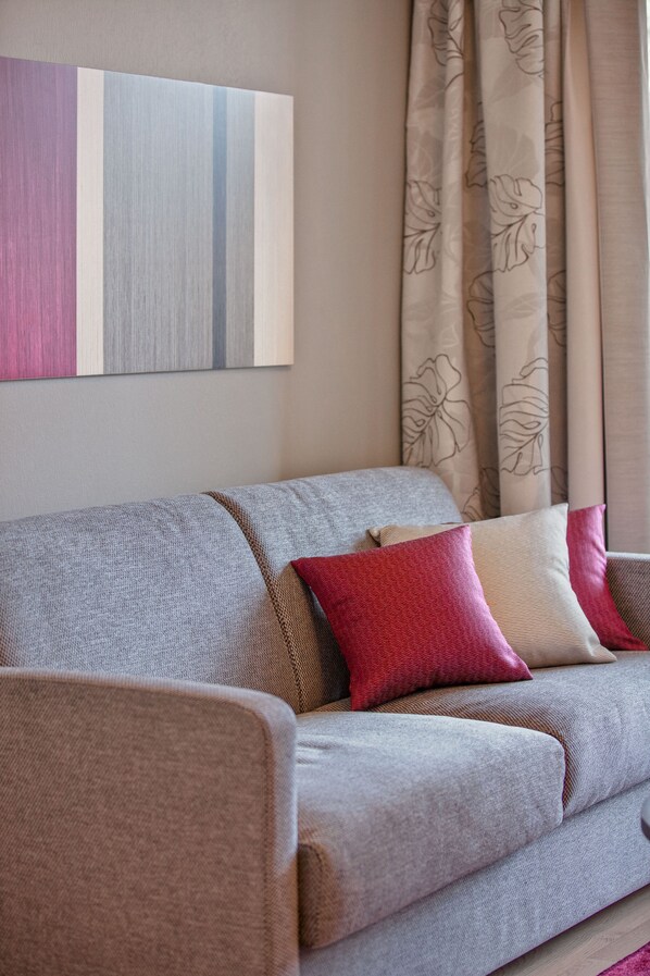 A sofa with a neutral color scheme, a floral-patterned curtain, and a piece of abstract art on the wall.