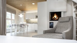 Ein modernes Wohnzimmer mit Kamin, weißen Möbeln und einer Küche im Hintergrund.