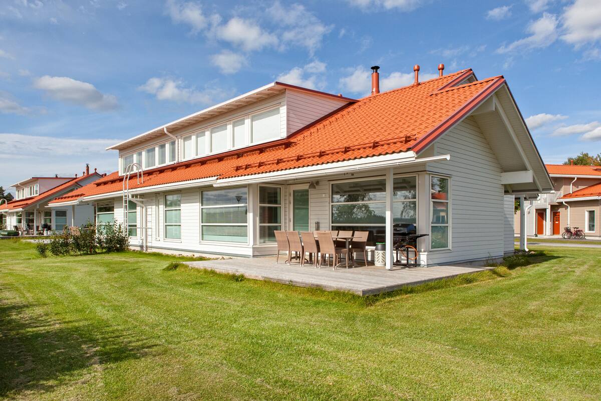 Ein modernes Haus mit rotem Dach, großen Fenstern und einer überdachten Terrasse mit Gartenmöbeln.