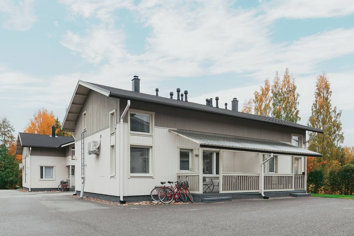 Ein modernes, zweistöckiges Haus mit einer überdachten Veranda, einem draußen abgestellten Fahrrad und blauem Himmel.