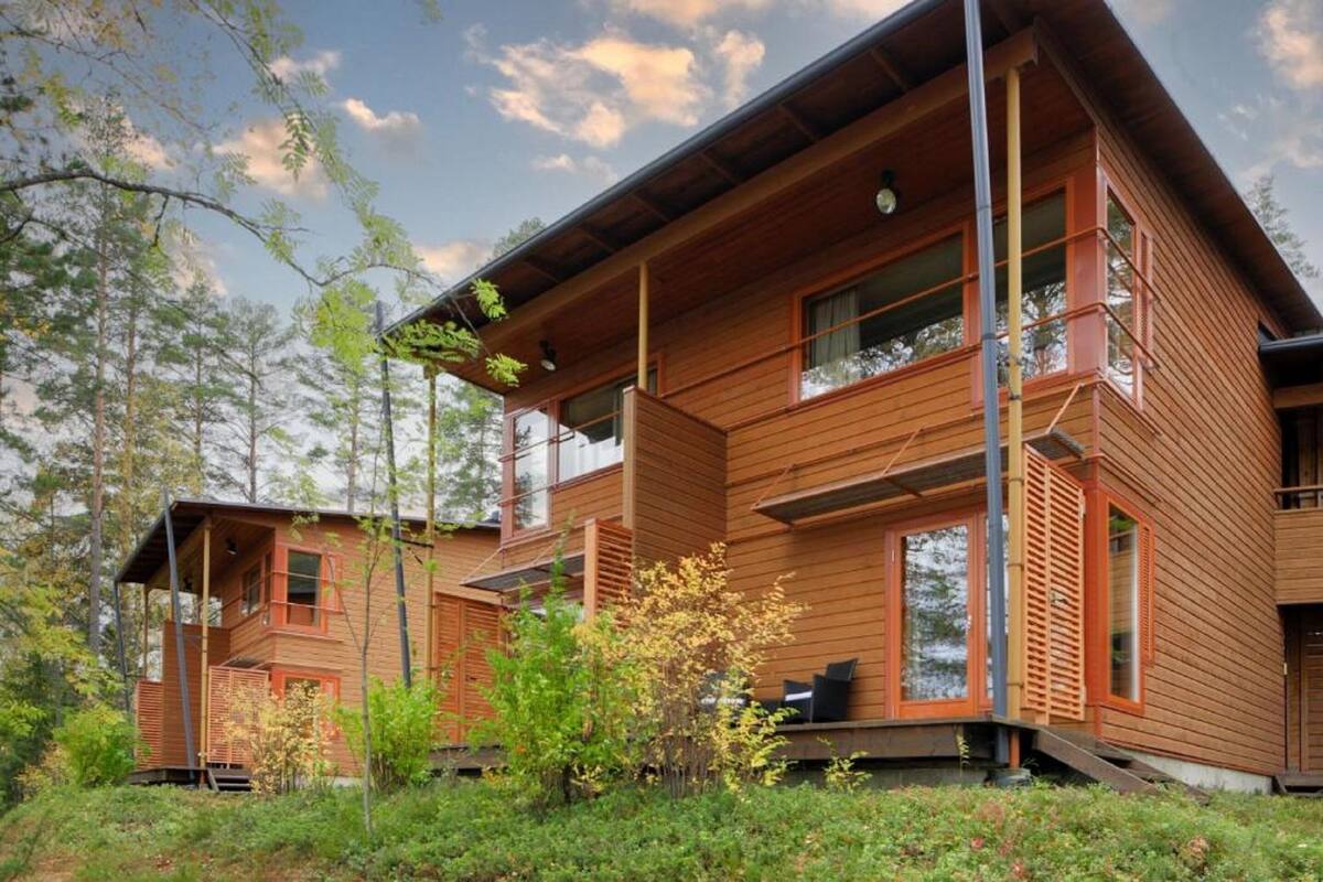 Eine moderne Holz-Blockhütte mit mehreren Ebenen, großen Fenstern und einem Balkon.