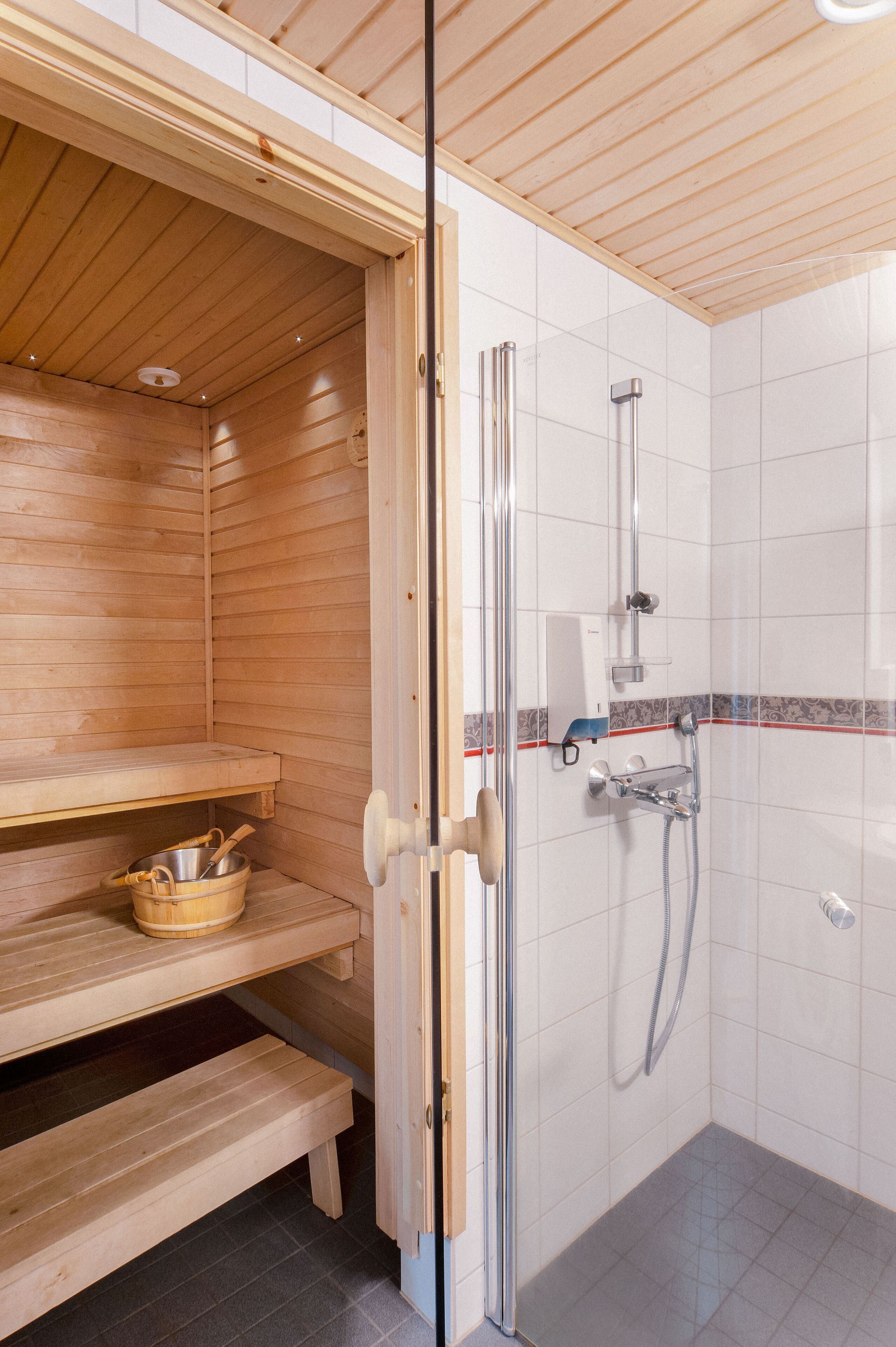 Una sauna con bancos de madera, una zona de ducha con puerta de vidrio y suelo de baldosas.