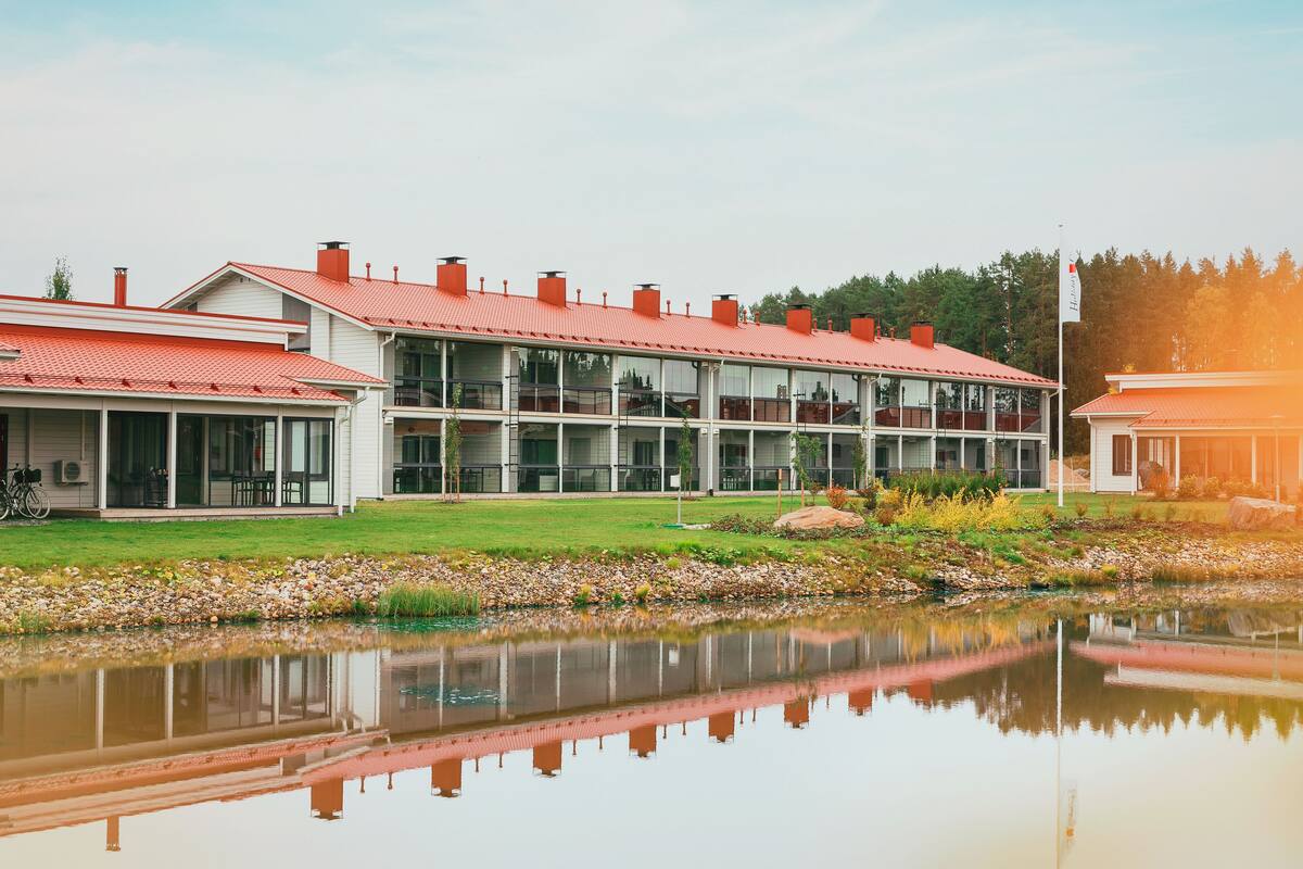 Ein modernes Gebäude mit rotem Dach, großen Fenstern und einem Spiegelbild in ruhigem Wasser.