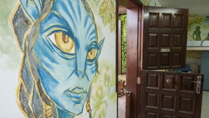 Un couloir orné d’une fresque représentant un chat bleu, avec une porte en bois et un sol carrelé.