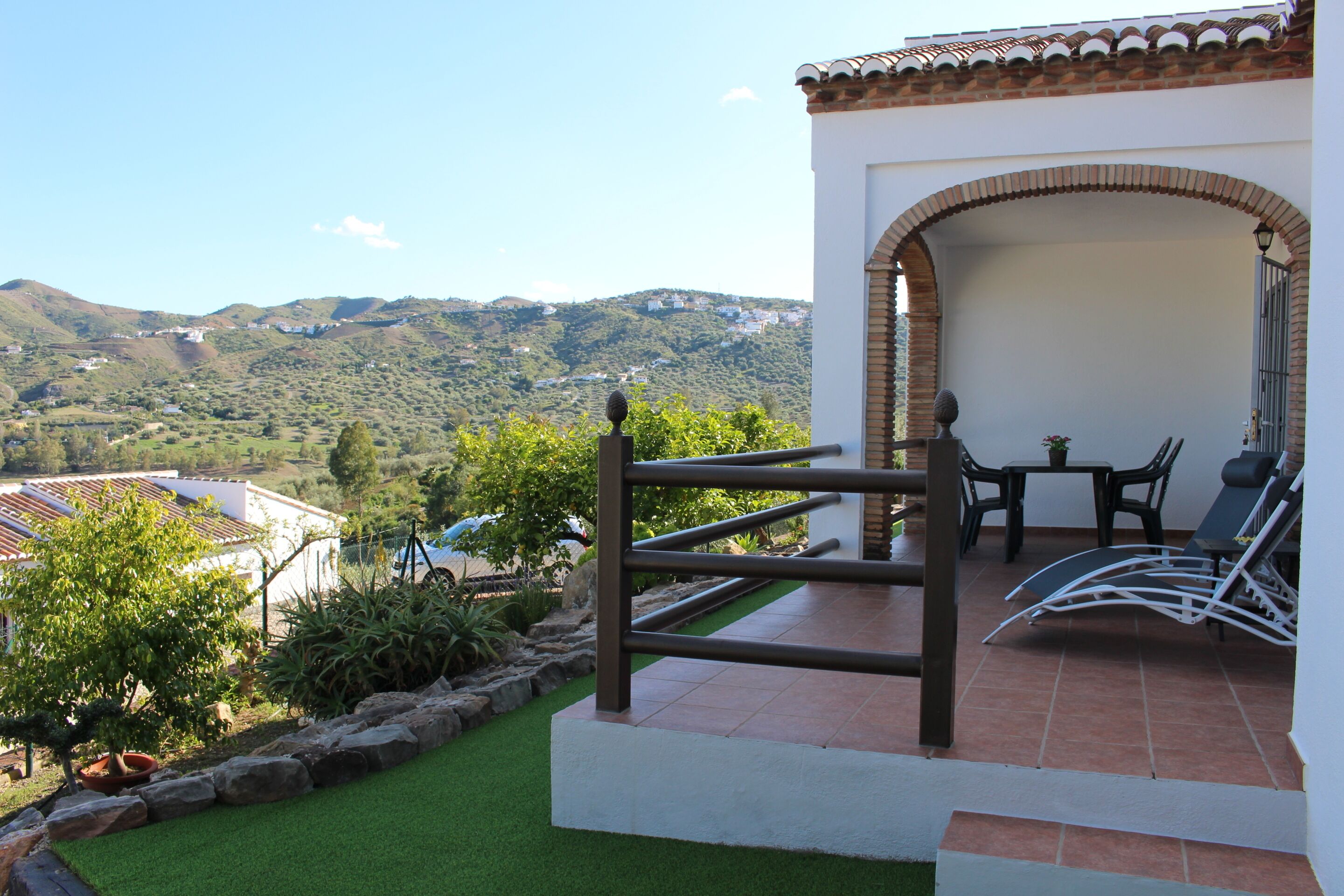 Une terrasse avec vue sur les collines, une table avec des chaises et un petit coin jardin.