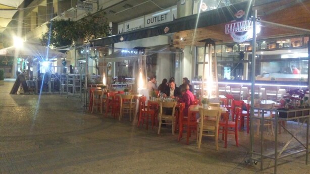 An outdoor dining area with tables and chairs, a sign for 'OUTLET', and a counter with a person behind it. - Ledras Town Center (Nicosia)