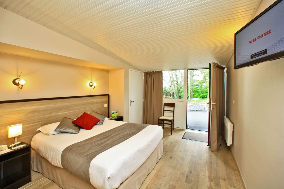 A hotel room with a bed, bedside lamps, a television displaying "WELCOME", and a view of greenery through the door.