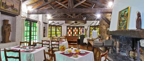A dining area with wooden tables and chairs, a stone wall with a statue, and a fireplace.