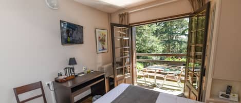 Habitación de hotel con cama, escritorio, silla y balcón con vistas a zonas verdes.