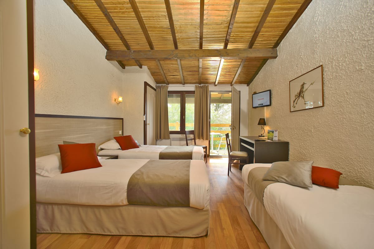 A hotel room with two beds, a desk, and a view of the outdoors.