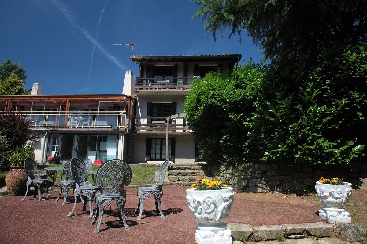 A two-story building with a balcony, outdoor seating area with metal chairs, and decorative planters.