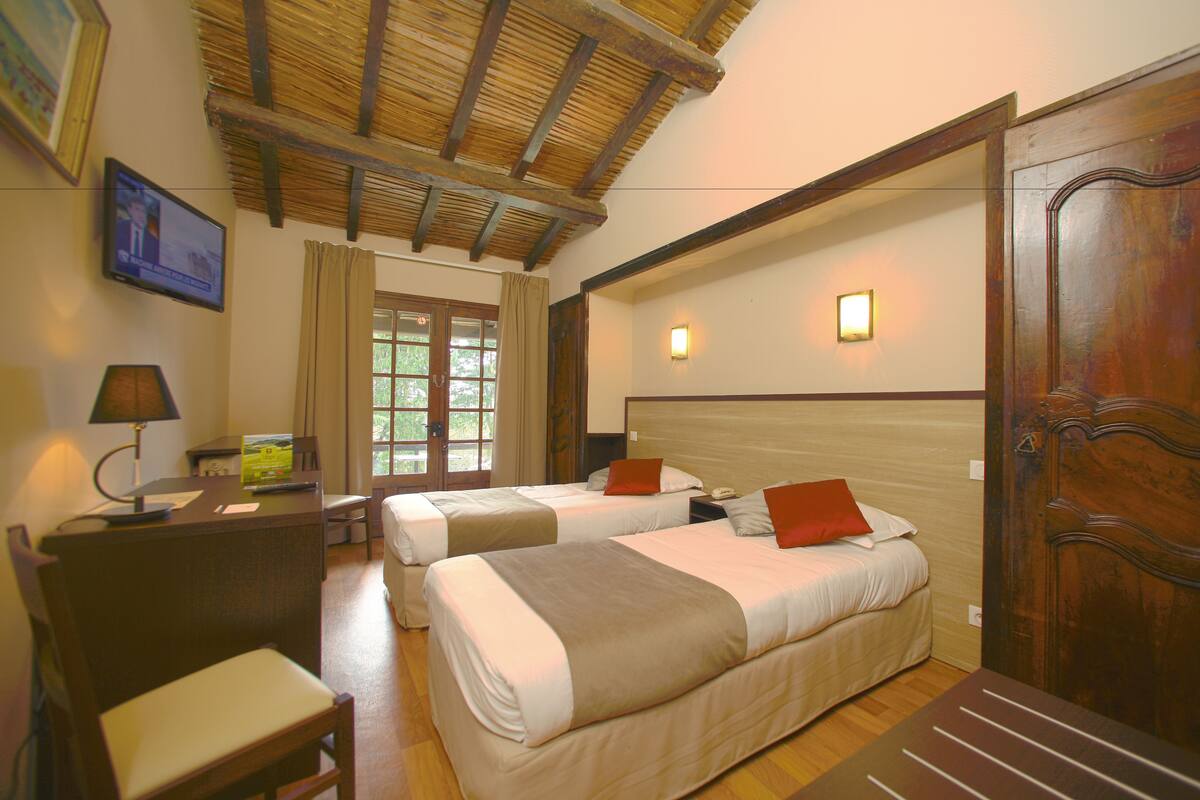 A hotel room with two beds, a desk with a lamp, a chair, and a wooden door.