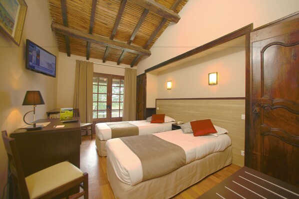 Una habitación de hotel con dos camas, un escritorio con lámpara, una silla y una puerta de madera.