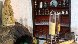 Une table de buffet garnie de divers plats, un mur en pierre orné d’une statue et des étagères remplies d’ustensiles de cuisine.