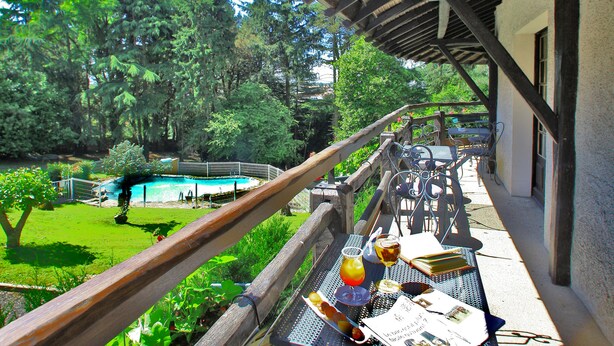 Un espace extérieur aménagé pour les repas, avec des tables et des chaises, une pergola en bois et une piscine en arrière-plan.