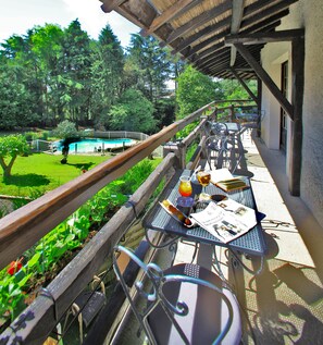 Un área de comedor al aire libre con mesas y sillas, una pérgola de madera y una piscina al fondo.