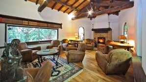 Un salon chaleureux avec des fauteuils en cuir, une cheminée et une grande fenêtre donnant sur une forêt.