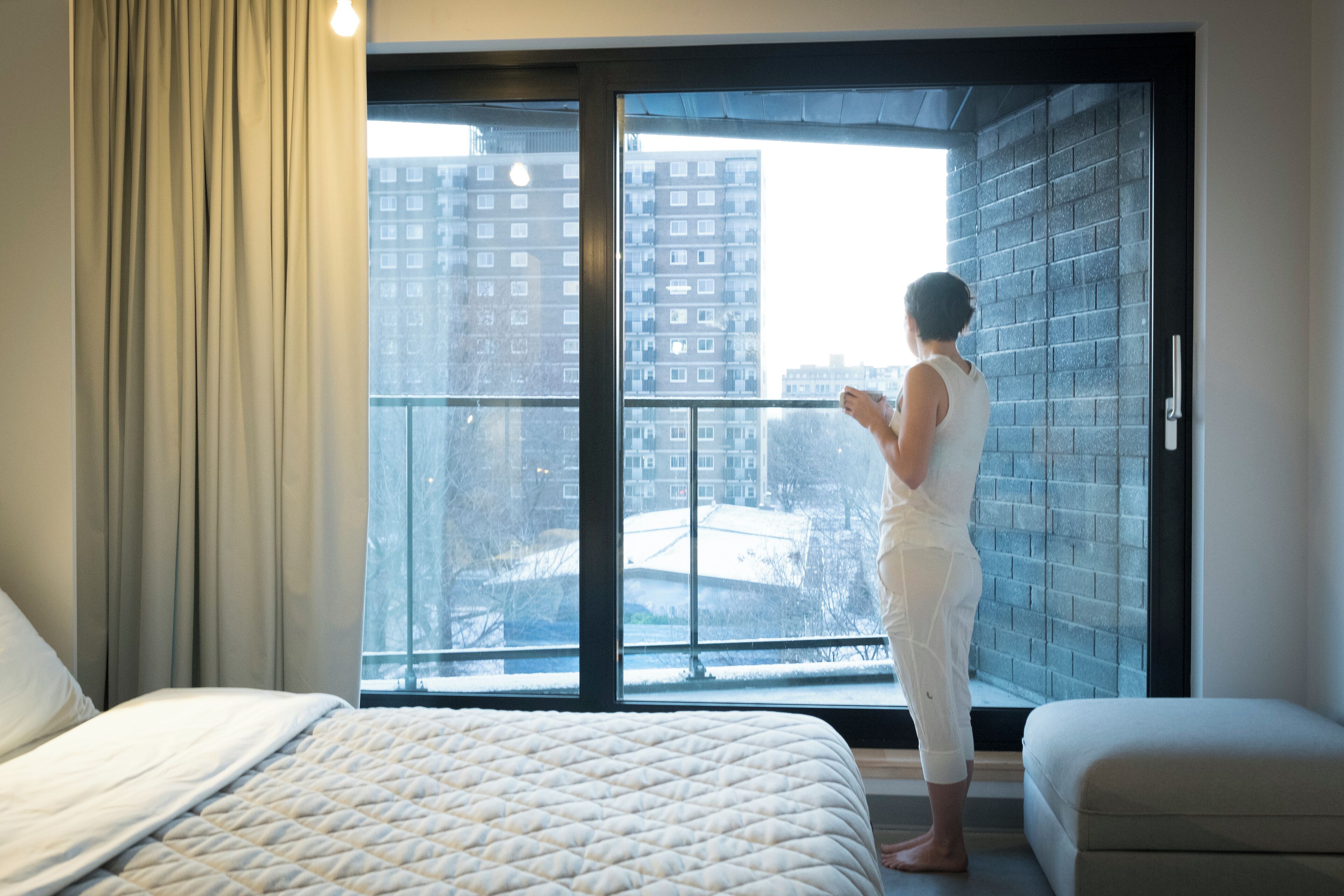 A bedroom with a large window, a bed, and a view of a cityscape.