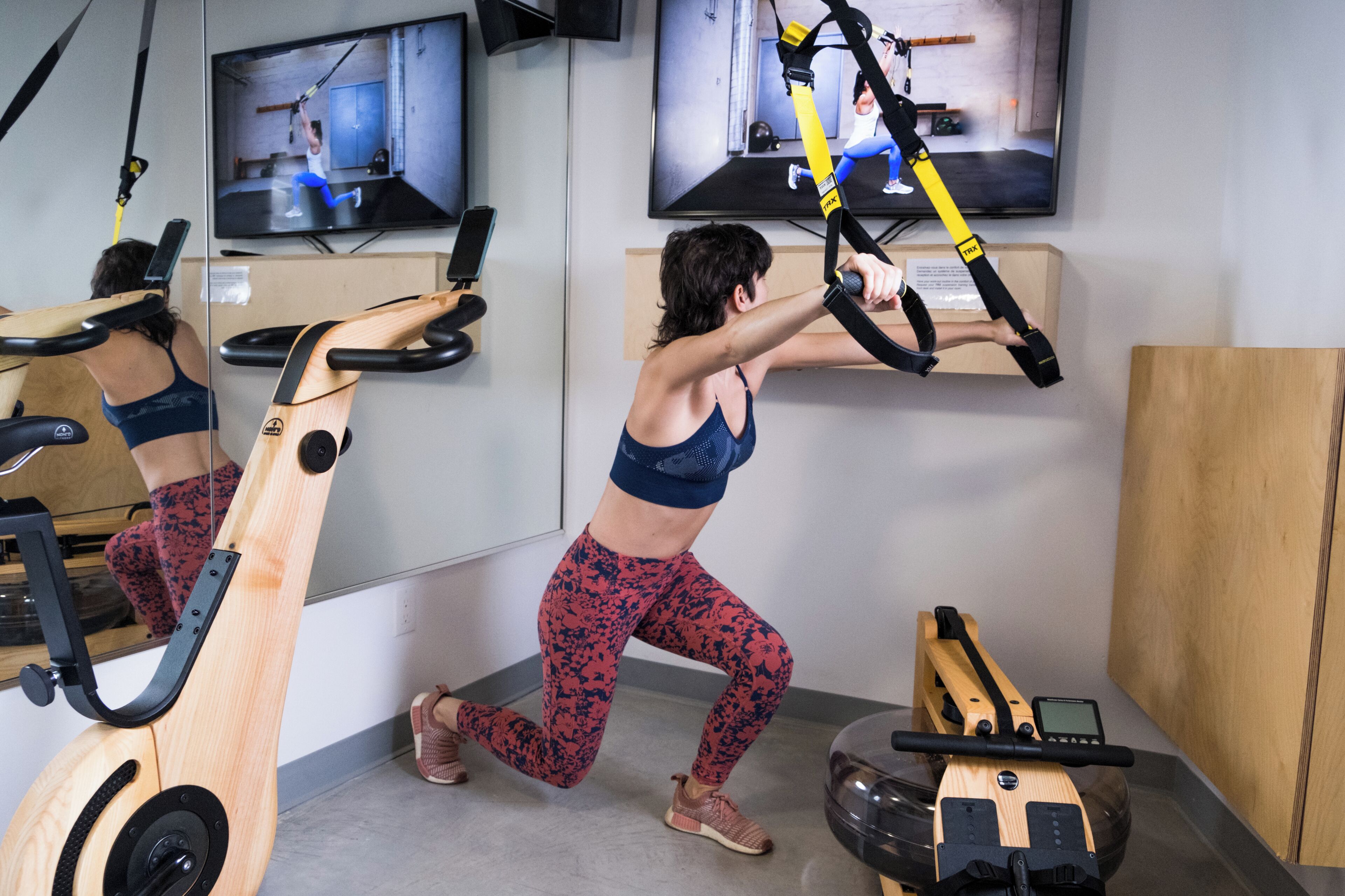 A gym with exercise equipment, a TV displaying workout videos, and a wooden cabinet.