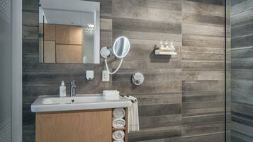 A modern bathroom with a wooden vanity, a large mirror, a built-in shelf with toiletries, and a glass shower enclosure.