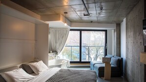 Une chambre moderne avec un grand lit, un coin salon avec un canapé et un ordinateur portable, une baignoire et une vue sur l’extérieur.