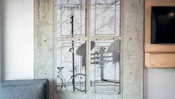 Une pièce avec un mur en béton, un téléviseur fixé au mur et quatre œuvres d’art encadrées représentant des bicyclettes et des arbres.