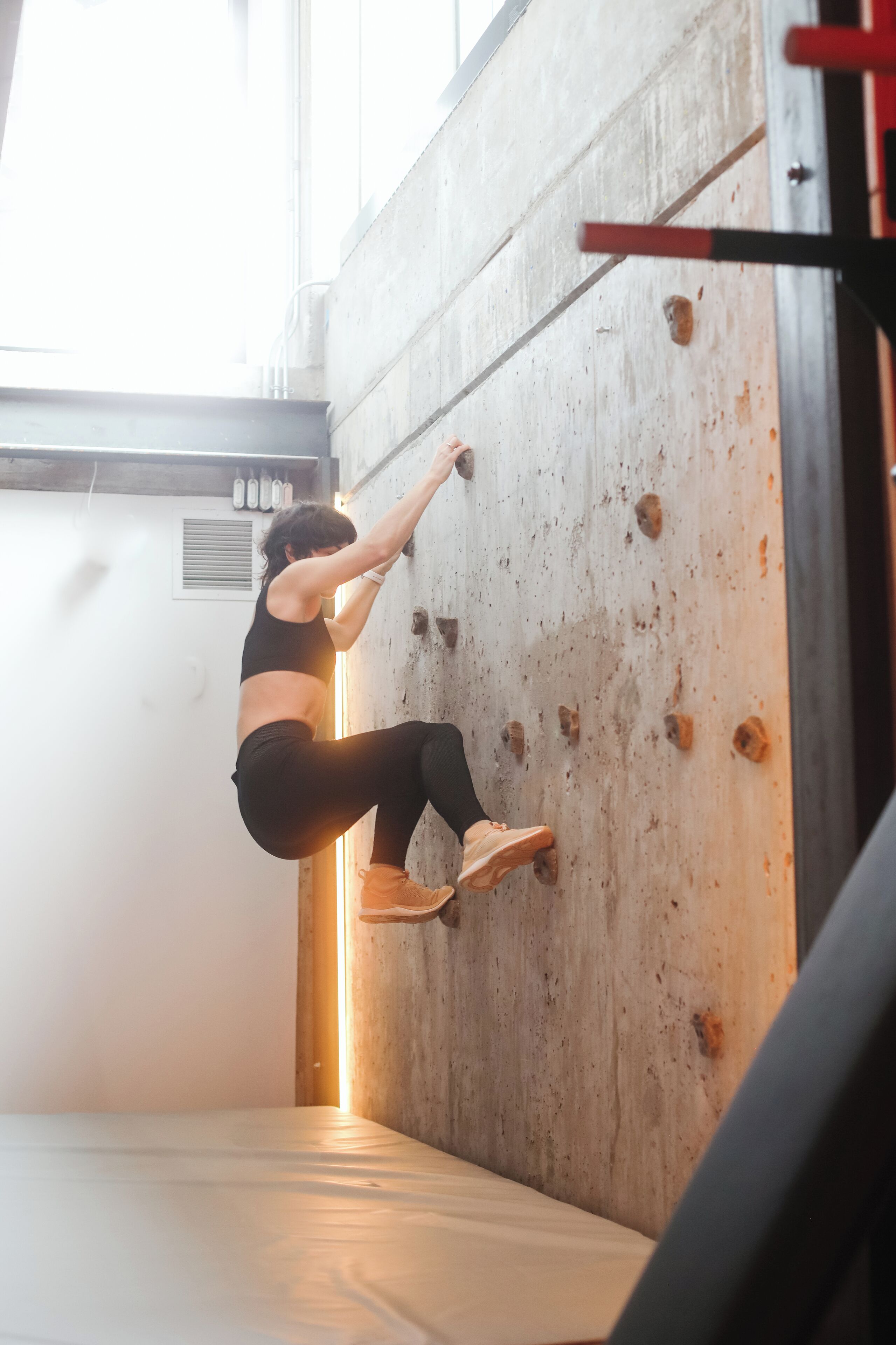 A person climbing a wooden wall in an indoor setting with a window and a bed visible.