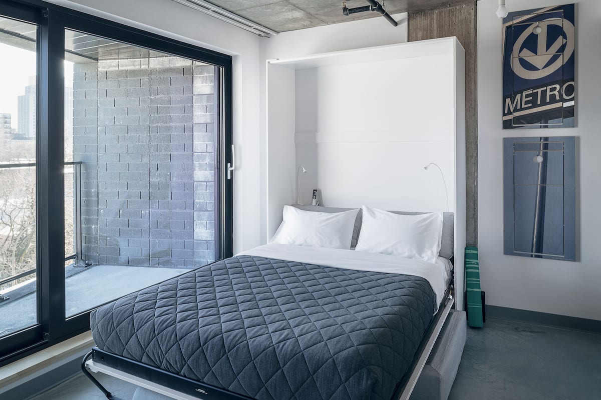A modern bedroom with a bed, a bathroom, and a view of the city.