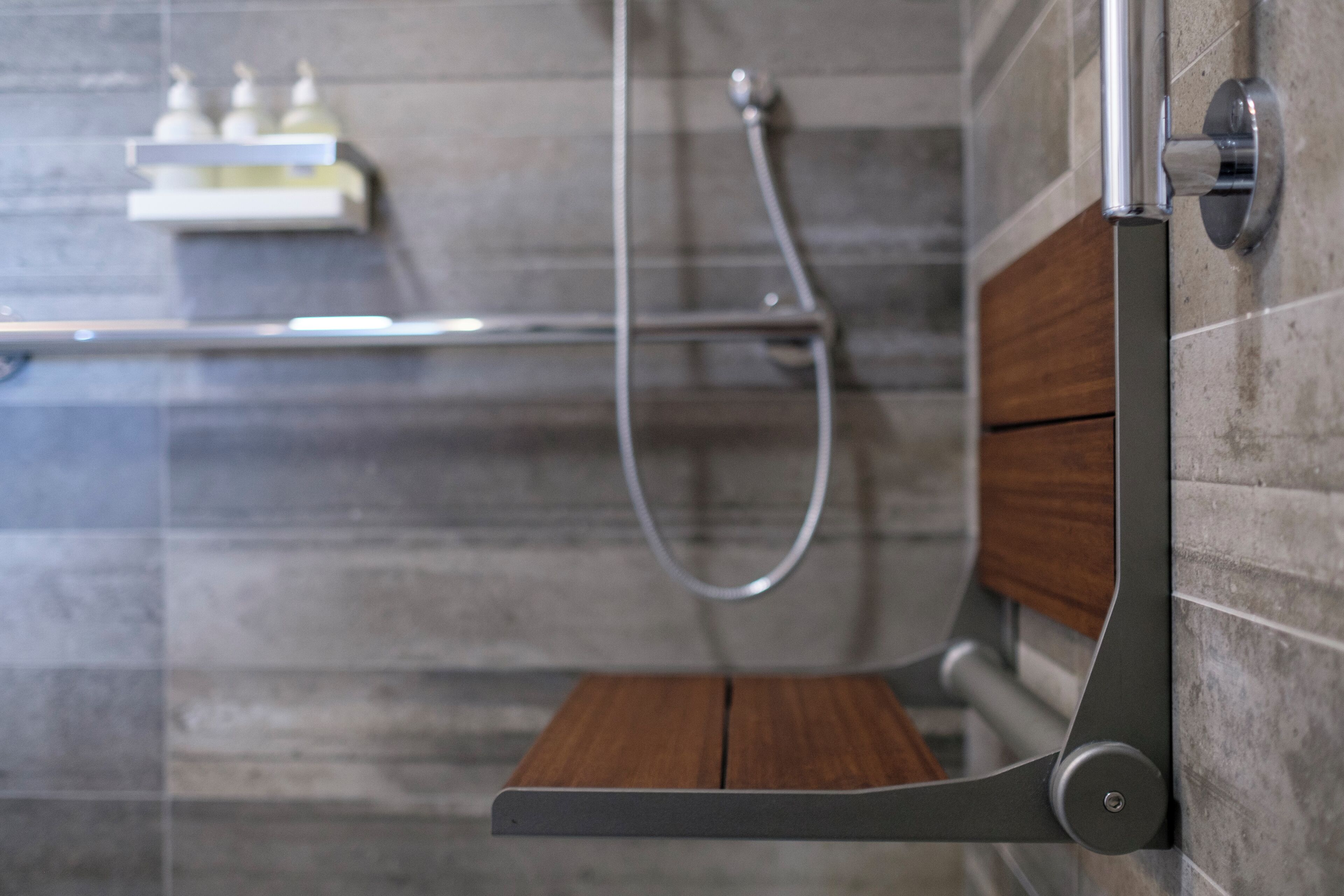 Un espace douche avec un banc en bois, un porte-serviettes et un distributeur de savon placé sur une étagère.