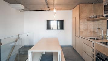 Uma cozinha moderna com uma mesa de madeira, forno embutido e televisão de tela plana presa na parede.
