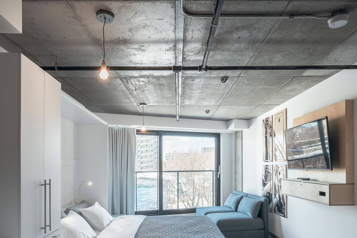 A modern bedroom with a bed, a seating area, a TV, and a view of the city.