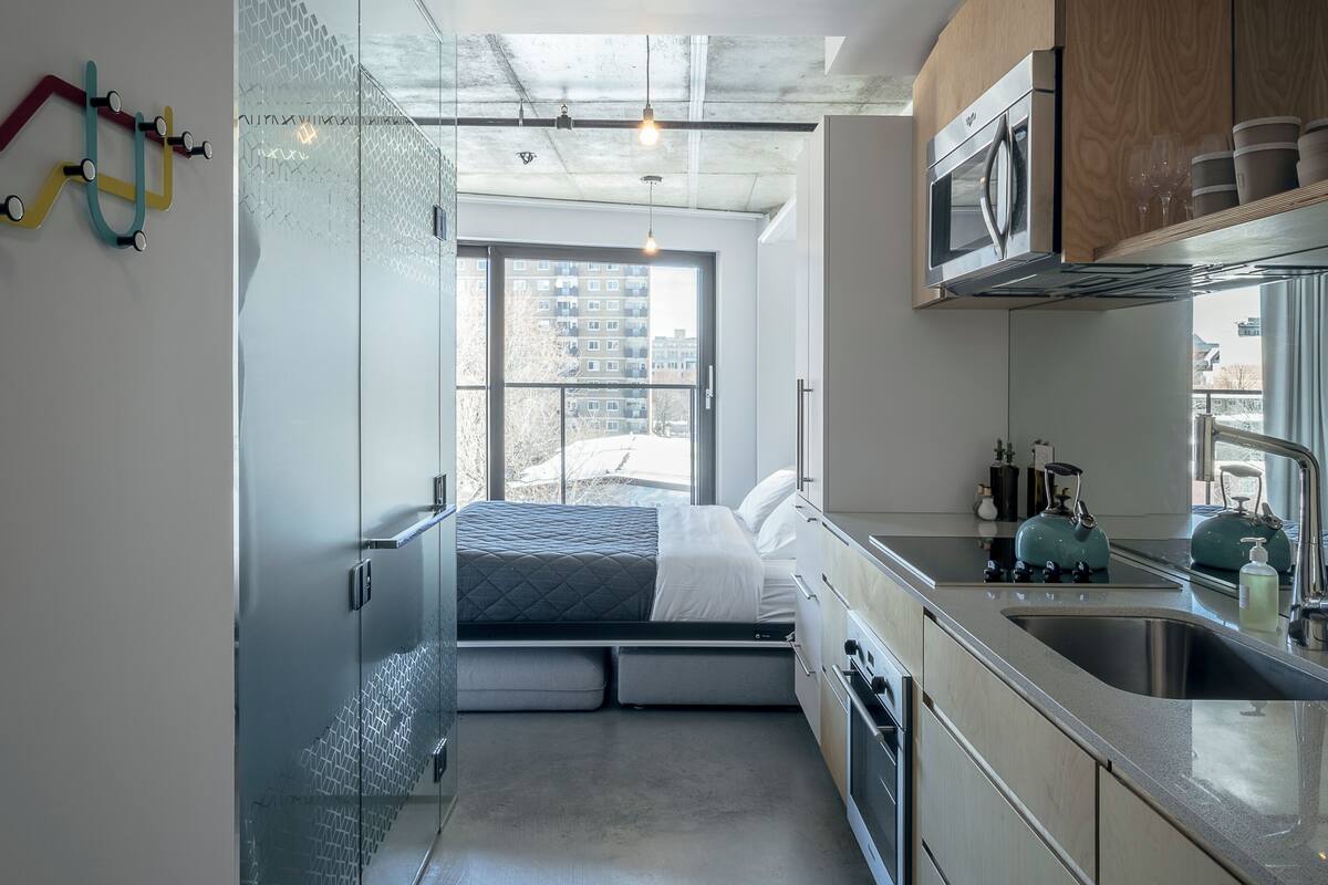A modern kitchen with a built-in bed, large windows, and a view of the city.