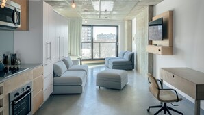 Une cuisine moderne dotée d’appareils électroménagers intégrés, un coin repas avec un canapé et un pouf, et un espace de travail avec un bureau et une chaise.
