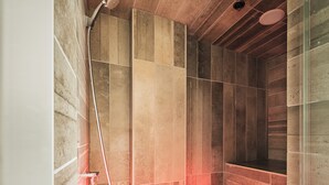 Une douche moderne avec un pare-douche en verre, une douchette à main et une lumière rouge au sol.
